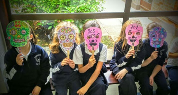 Pupils holding up painted masks they made in art class